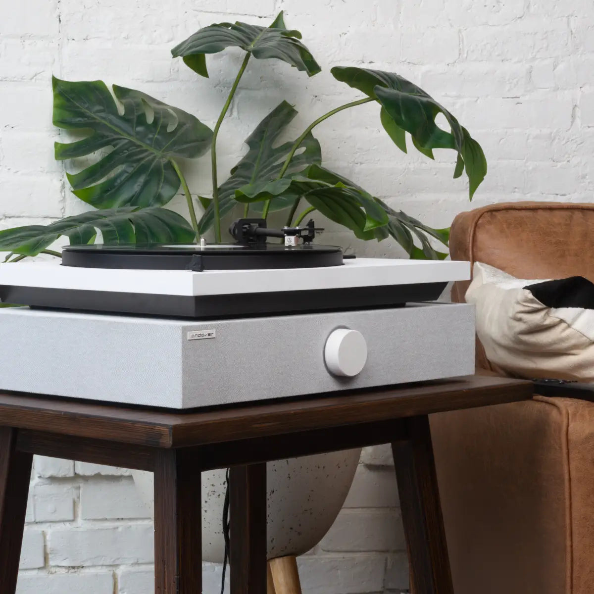 White Andover Audio SpinBase 2 beneath a turntable on a wooden table beside an armchair.