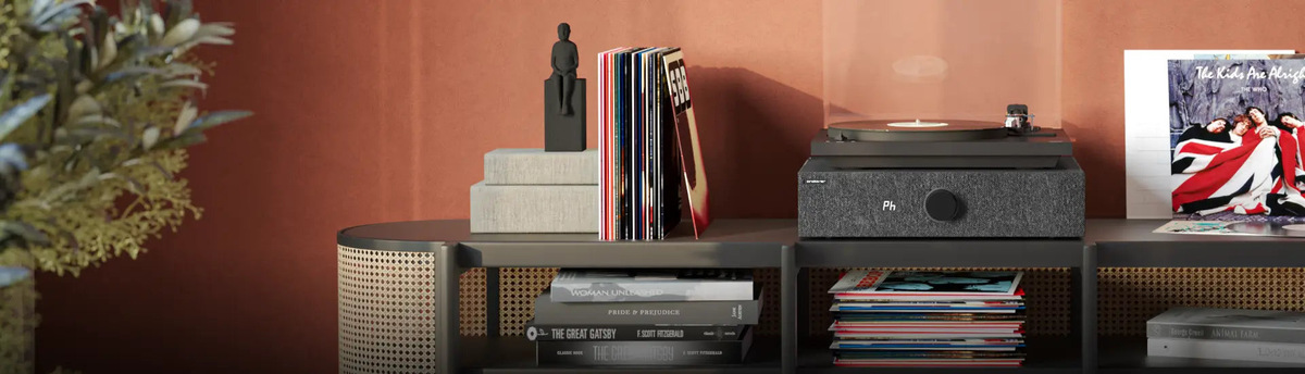 Black SpinBase MAX 2 and turntable on an open media unit beside records.