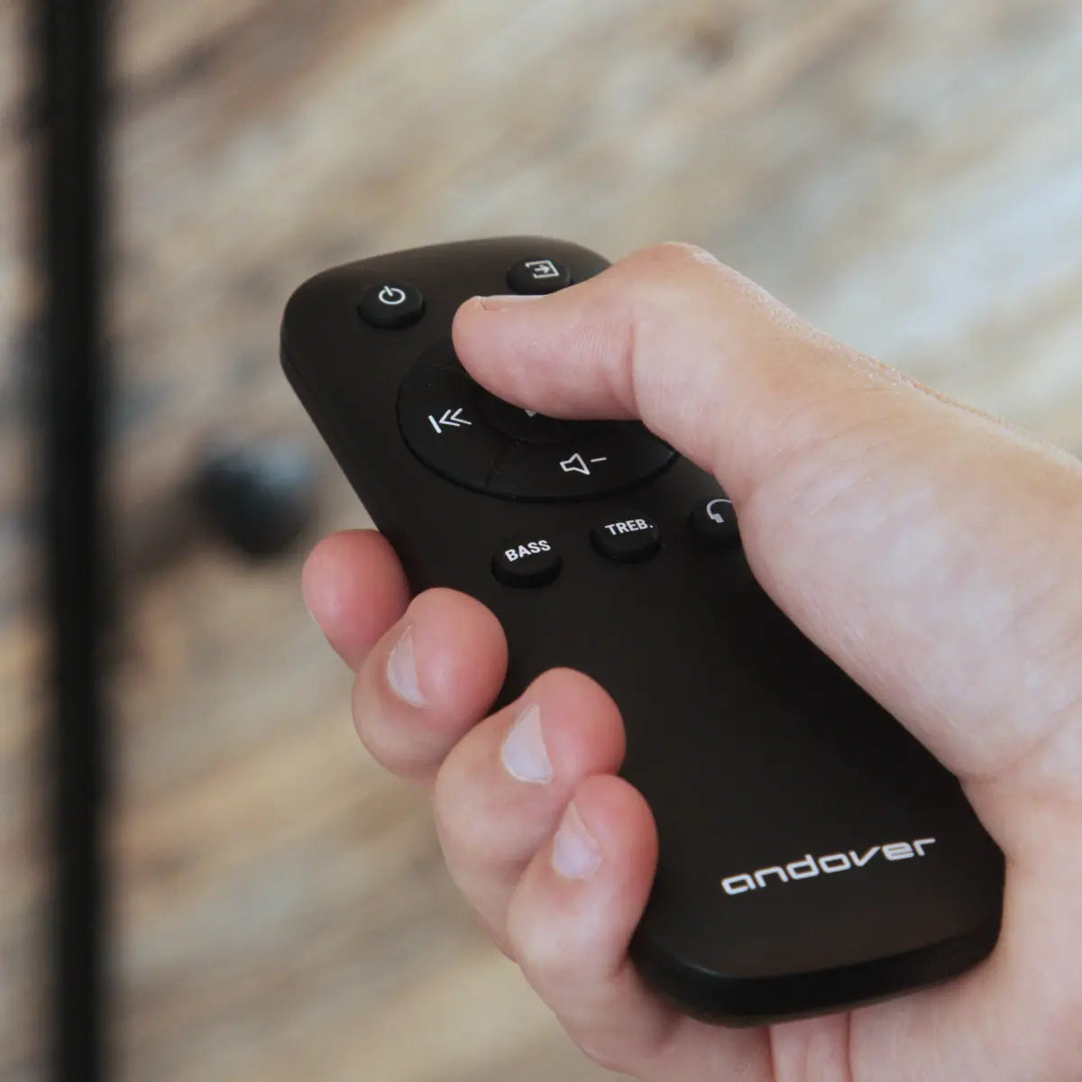 Hand holding the Andover remote with volume, source, bass and treble controls.