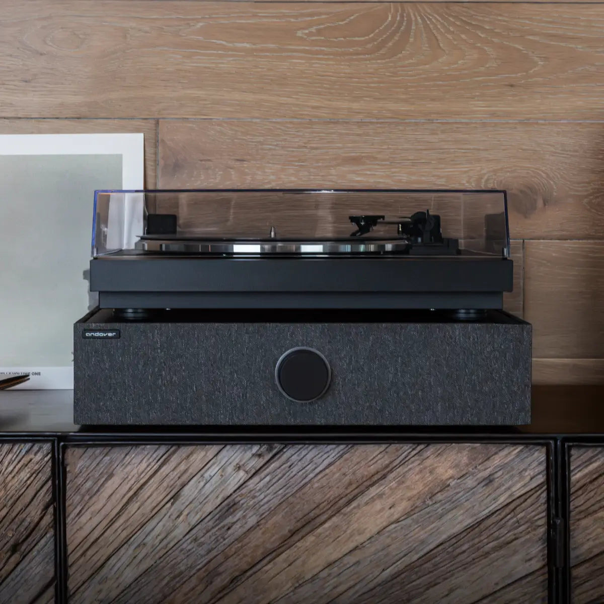 Black SpinBase MAX 2 beneath a turntable with its dustcover raised on a media console.