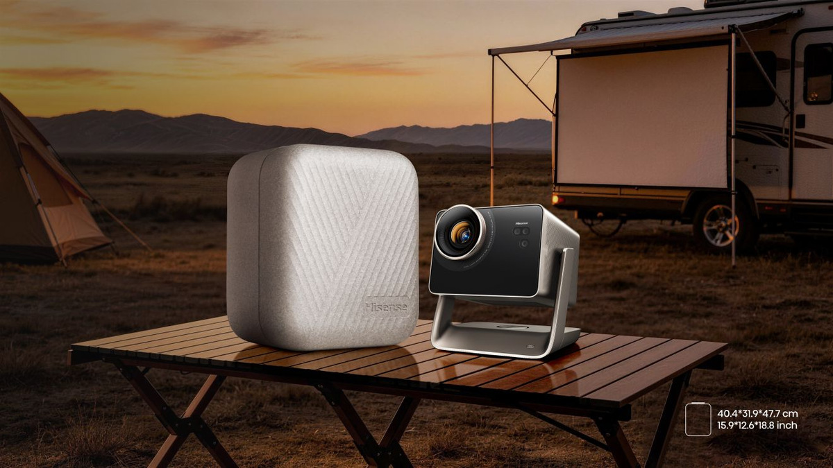 Projector beside a light-coloured carrycase on a camping table, with a campervan and projection screen behind.